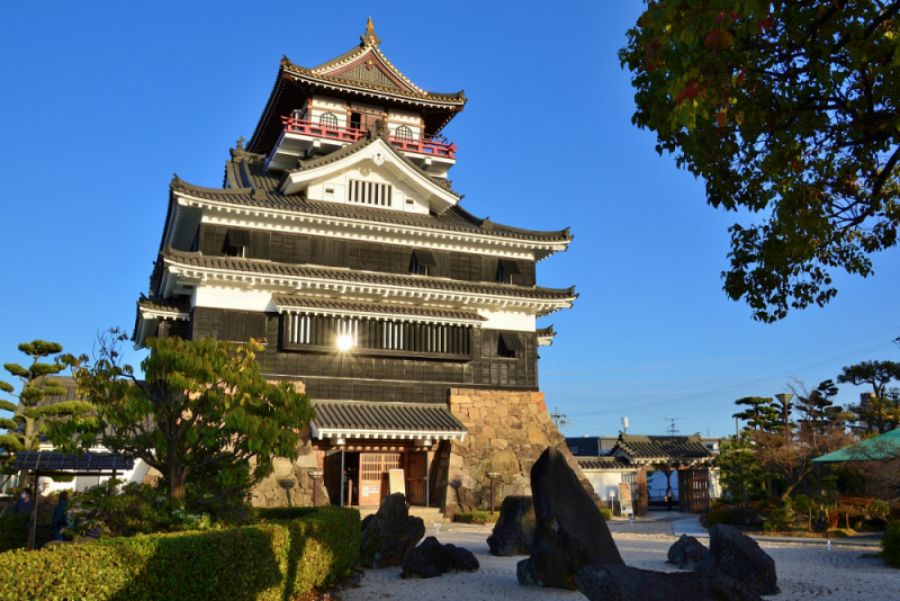 青空を背景に、石垣の上に建つ清洲城天主閣の近景。黒い外壁と赤い高欄が特徴的な再建天守。