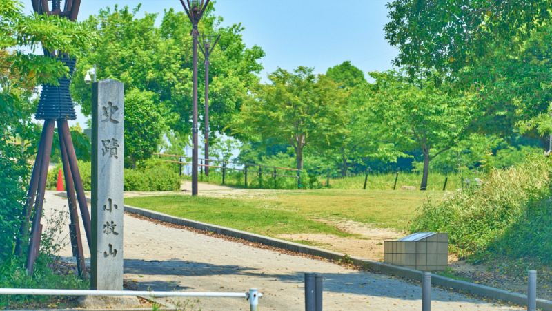 「史跡 小牧山」と刻まれた大きな石碑が立つ、整備された公園の入り口付近の風景。
