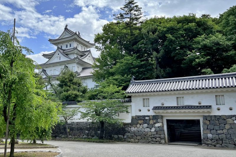 石垣の上に堂々と建つ白壁の櫓門と、その奥にそびえ立つ大垣城の四層天守。生い茂る木々の緑に映える、堅牢な城郭構造を捉えた風景。