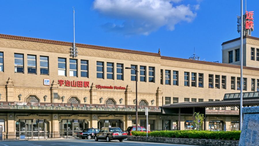 登録有形文化財である宇治山田駅の壮麗なテラコッタ建築の駅舎。駅前ロータリーにはタクシーが停車しており、右奥には近鉄の赤いロゴ看板が見える。