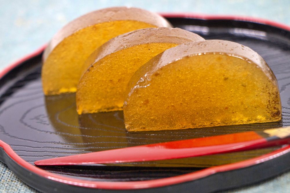 黒い盆に並べられた、半月型の美しい琥珀色の柿羊羹。柿の風味が凝縮された艶やかな質感と、歴史ある城下町・大垣の伝統を感じさせる上品な佇まい。