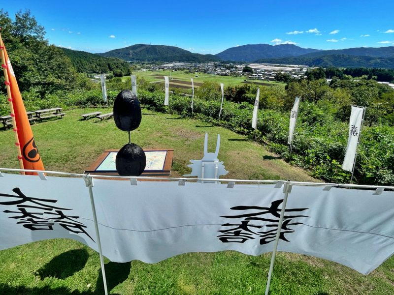石田三成の本陣跡がある笹尾山山頂からの風景。手前に「大一大万大吉」の旗印と馬防柵があり、奥には関ケ原の田園地帯と山々が広がる様子。