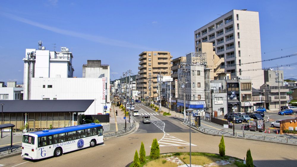 犬山駅周辺の整備された道路と、青空の下に停車する路面バスやビル群の風景