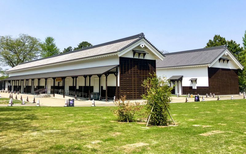 青空と芝生の広場の奥に建つ、和風建築の西の丸御蔵城宝館の外観。