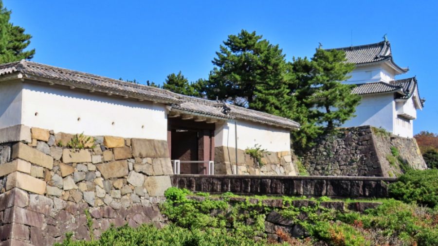 青空を背景に建つ名古屋城の表二之門と重要文化財の隅櫓。手前には重厚で美しい石垣が積まれている。