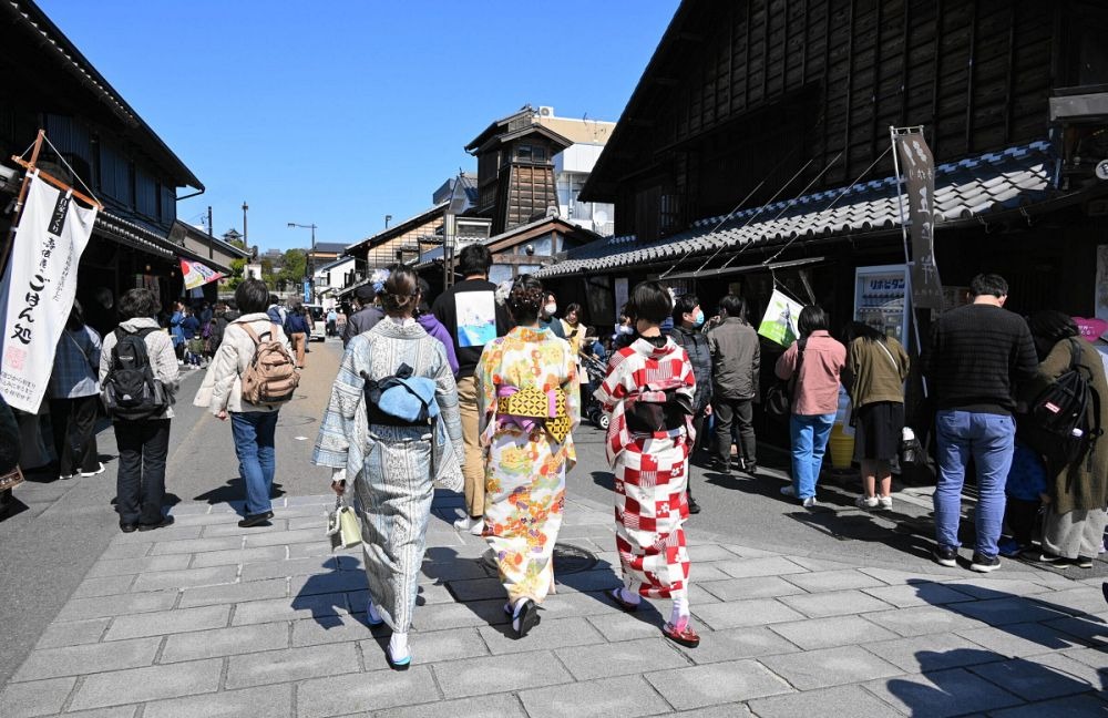 青空の下、古い町家が並ぶ犬山城下町を歩く着物姿の女性たちと観光客の様子。