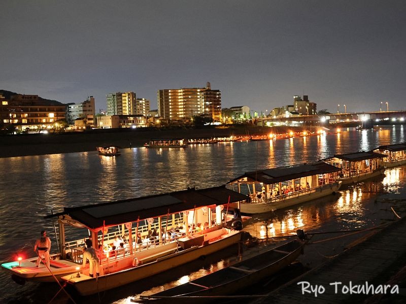 夜の長良川に並ぶ、観光客を乗せた複数の屋形船。背景には岐阜市街地の明かりが見える。
