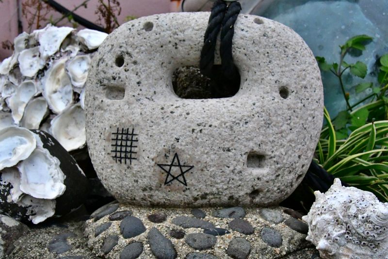 海女が使う石の重石。表面に格子状の「ドーマン」と星形の「セーマン」の紋様が手書きされており、周囲には貝殻が供えられている。