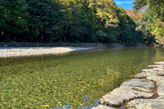 澄んだ水が流れる五十鈴川と、川岸に敷き詰められた平らな石畳。背景には豊かな森が広がっています。