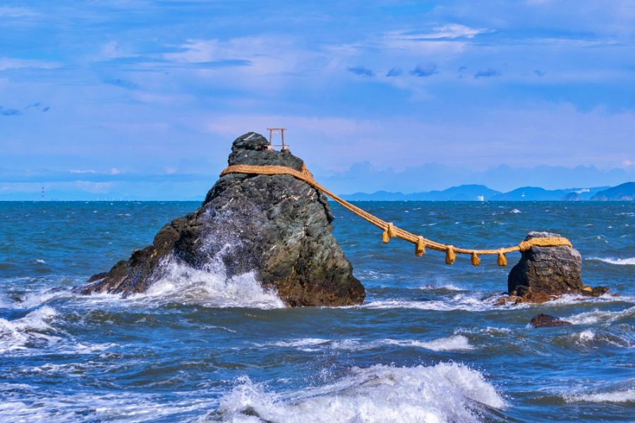 青い海の中に、太い注連縄で結ばれた大小2つの岩（夫婦岩）。白い波が岩肌に激しく当たっている。