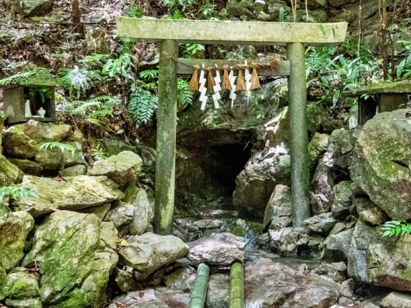 苔むした岩場と豊かな緑に囲まれた、天の岩戸の入り口に立つ石造りの鳥居